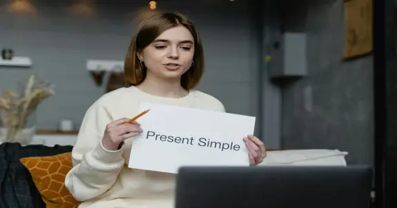 Lehrerin zeigt im video unterricht ein schild mit present simple