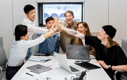 数人がテーブルを囲んで、Teamsのホワイトボードの使い方について会議をしています。