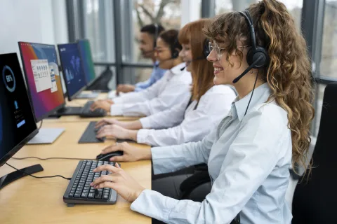 Busy open-plan office where support teams use professional contact center headsets to maintain high call quality amidst background noise.