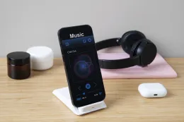 High-angle view of a modern desk setup featuring a smartphone playing music on a charging stand, over-ear headphones in the background, and a wireless earbud case on the table, illustrating a clean workspace ideal for the best wireless earbuds for Android users.