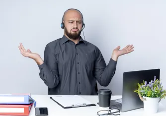 A frustrated person sitting at a desk, looking at a laptop with headphones on, troubleshooting why their headphones are not working
