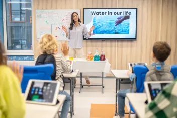 woman standing children sitting desks